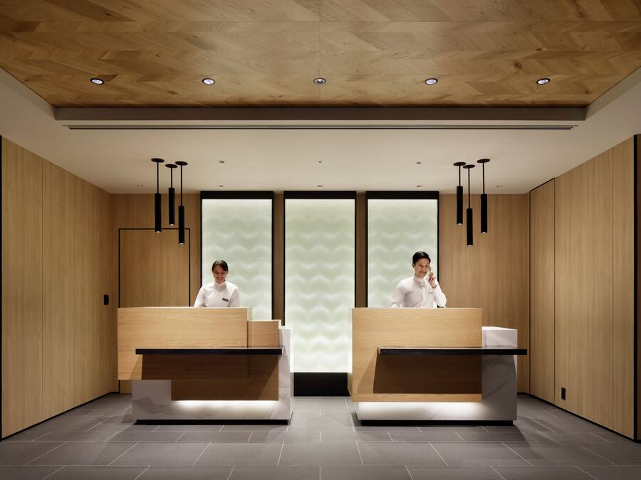 A modern hotel reception area with wooden paneling, two reception desks, and pendant lighting.