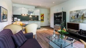 A modern living room with a sofa, coffee table, and TV. There is a kitchen in the background with cabinets and a dining area. - Villa Höger Whg. 06, Deutschland (Ostseebad Boltenhagen)