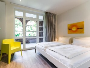 Un dormitorio con un ventanal grande, una silla amarilla y una cama con ropa de cama blanca.