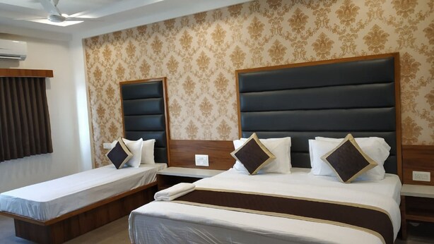 A hotel room with two single beds and a larger bed, all with headboards and pillows. - Hotel Govindam by Sky Stays (Ahmedabad)