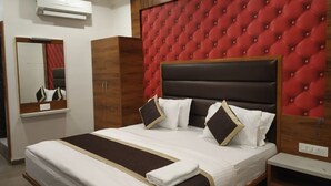 A hotel room with a large bed, a red tufted headboard, a mirror, and a wardrobe. - Hotel Govindam by Sky Stays (Ahmedabad)