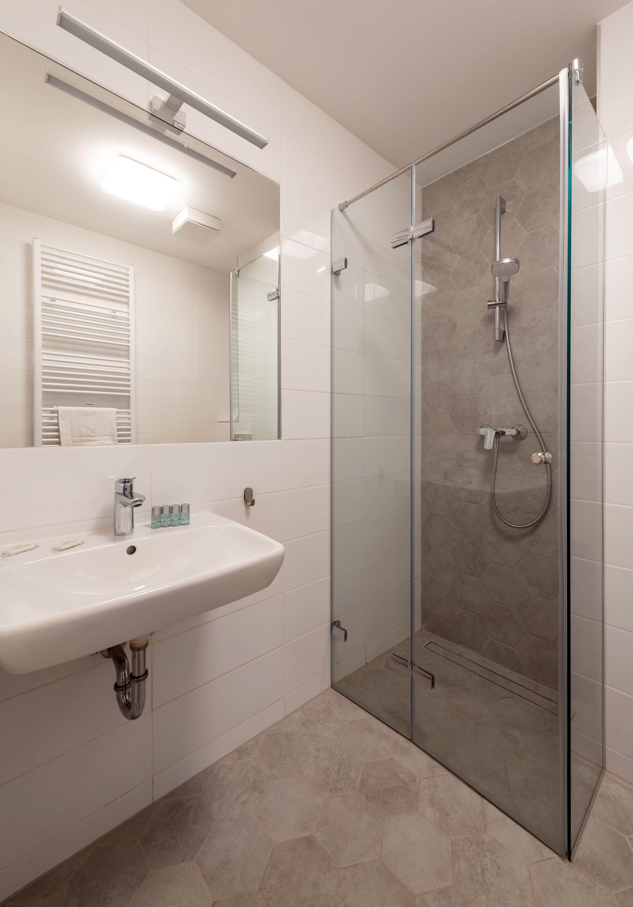 Een moderne badkamer met een douche in een glazen cabine, een wit wastafelmeubel en een spiegel erboven.