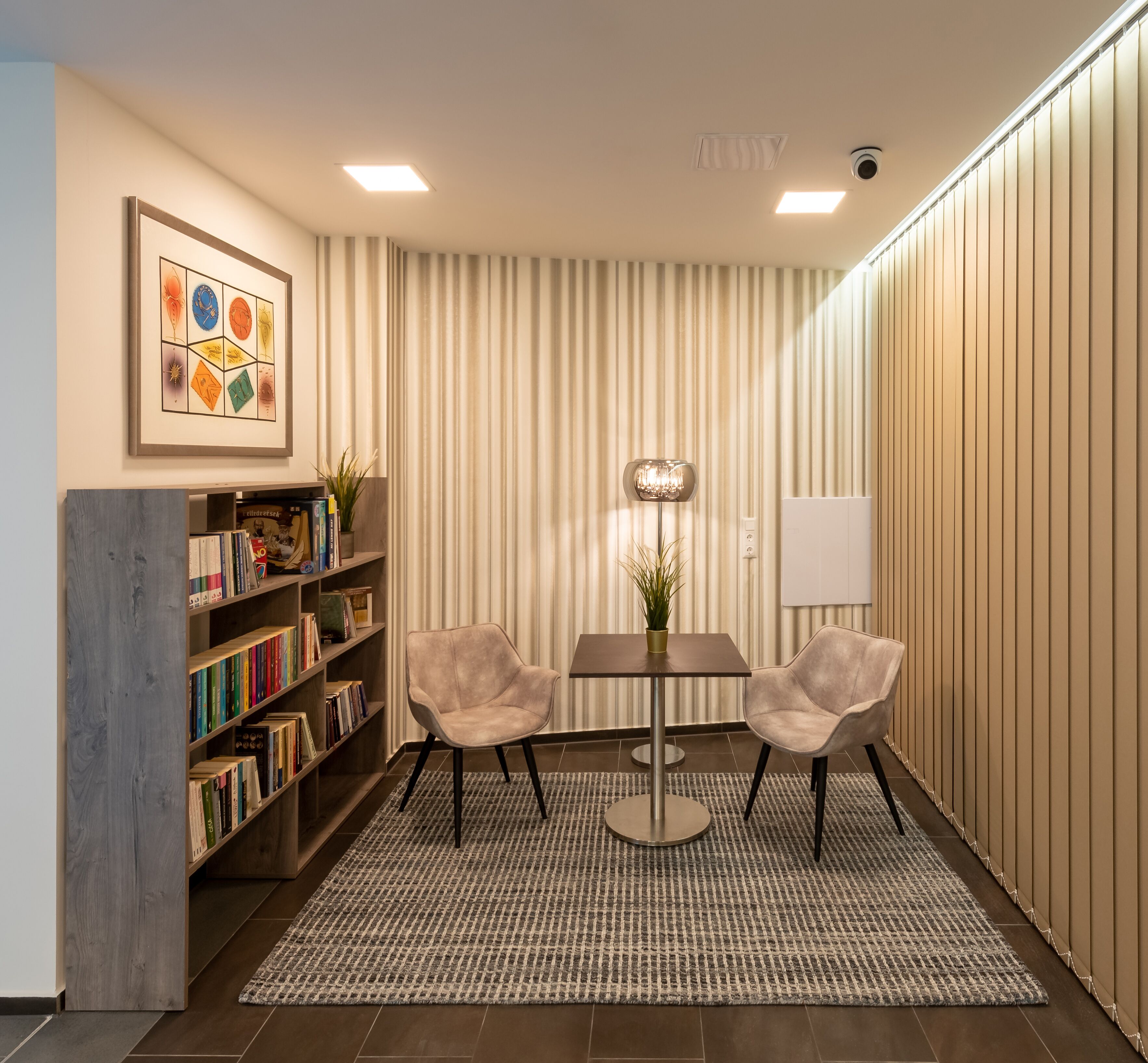 Un área de espera moderna con estantería, dos sillones, una mesa y un tapete estampado.