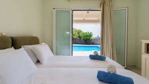 A bedroom with a bed, pillows, a bedside table, and a view of a swimming pool.