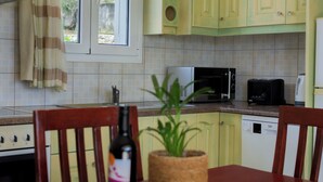 A kitchen with a microwave, toaster, and dishwasher. There is a bottle of wine and a plant on the table.
