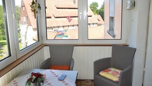 Una habitación con dos sillas de mimbre, una mesa con mantel floreado y vistas a un edificio con tejado de baldosas.
