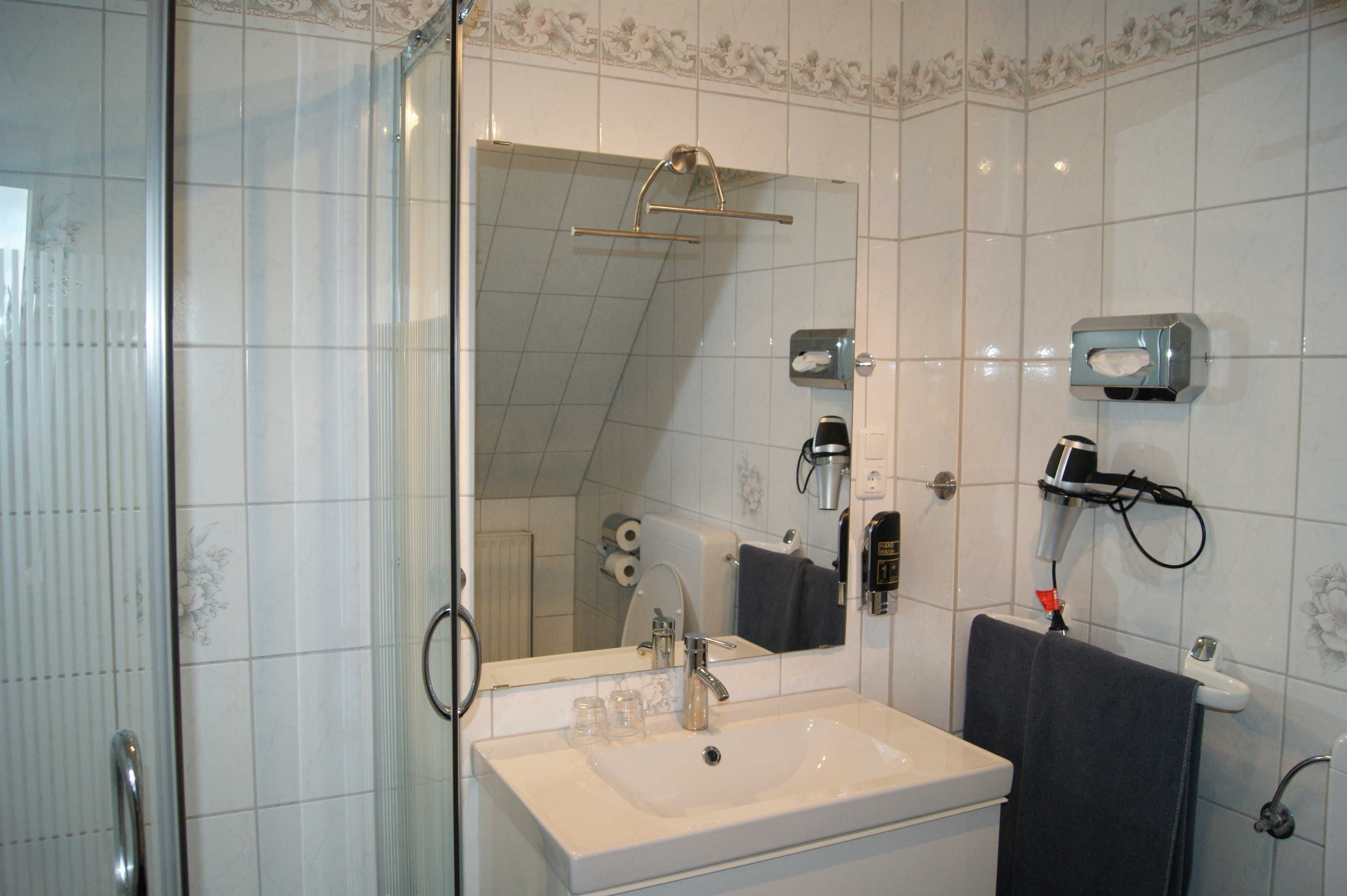 Ein Badezimmer mit einem weißen Waschbecken, einem Spiegel, einem Handtuchhalter und einer Duschkabine.