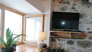 Quarto com parede de pedra, bancada de madeira, televisão e janela.