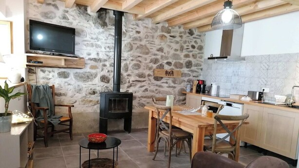 Uma sala de estar aconchegante com parede de pedra, televisão, lareira e mesa de jantar de madeira.