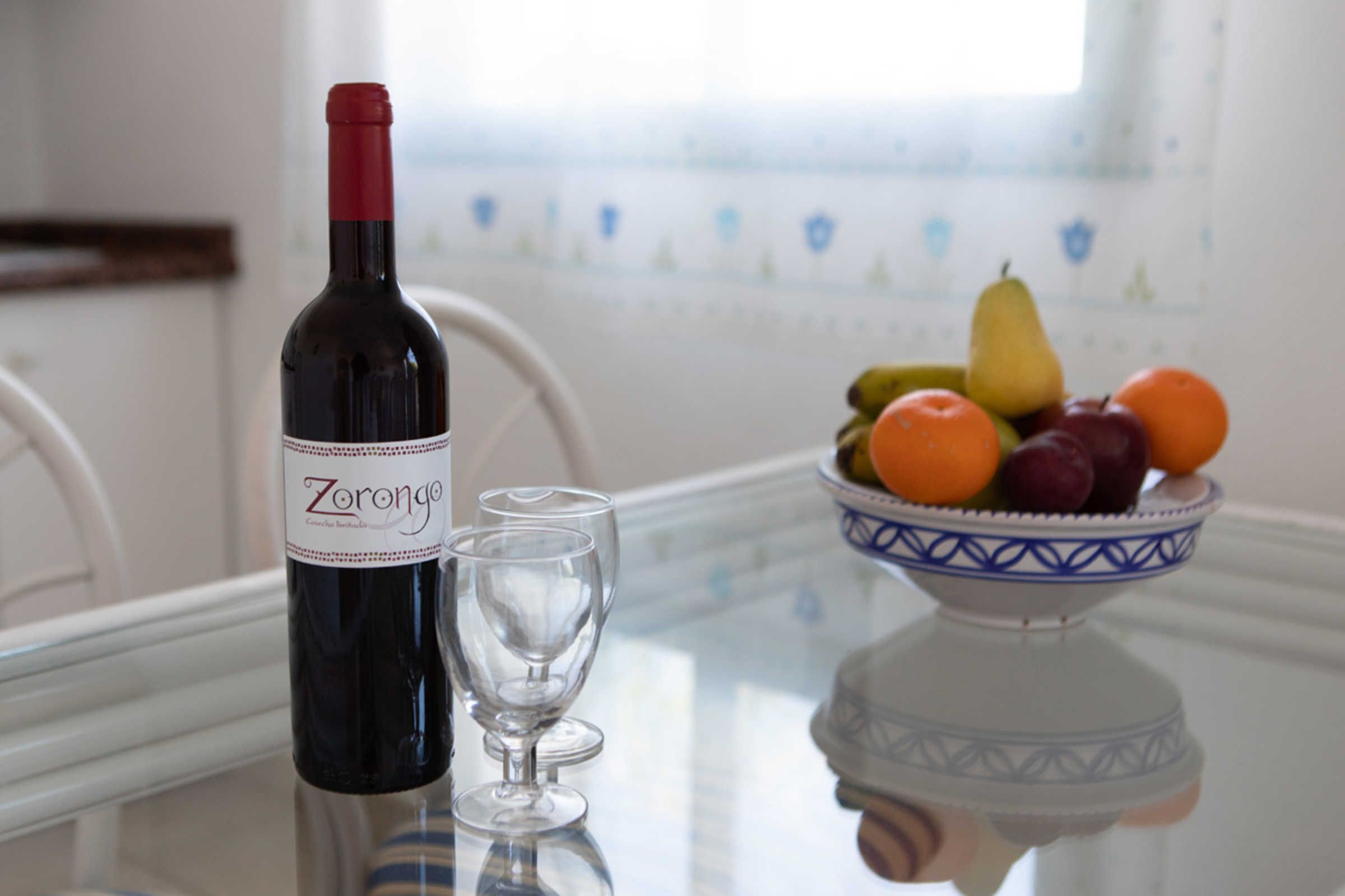A bottle of Zorongo wine, a glass, and a bowl of fruit on a table.