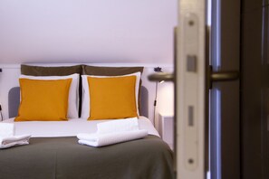 A hotel room with a bed, two pillows, a folded towel, and a door.
