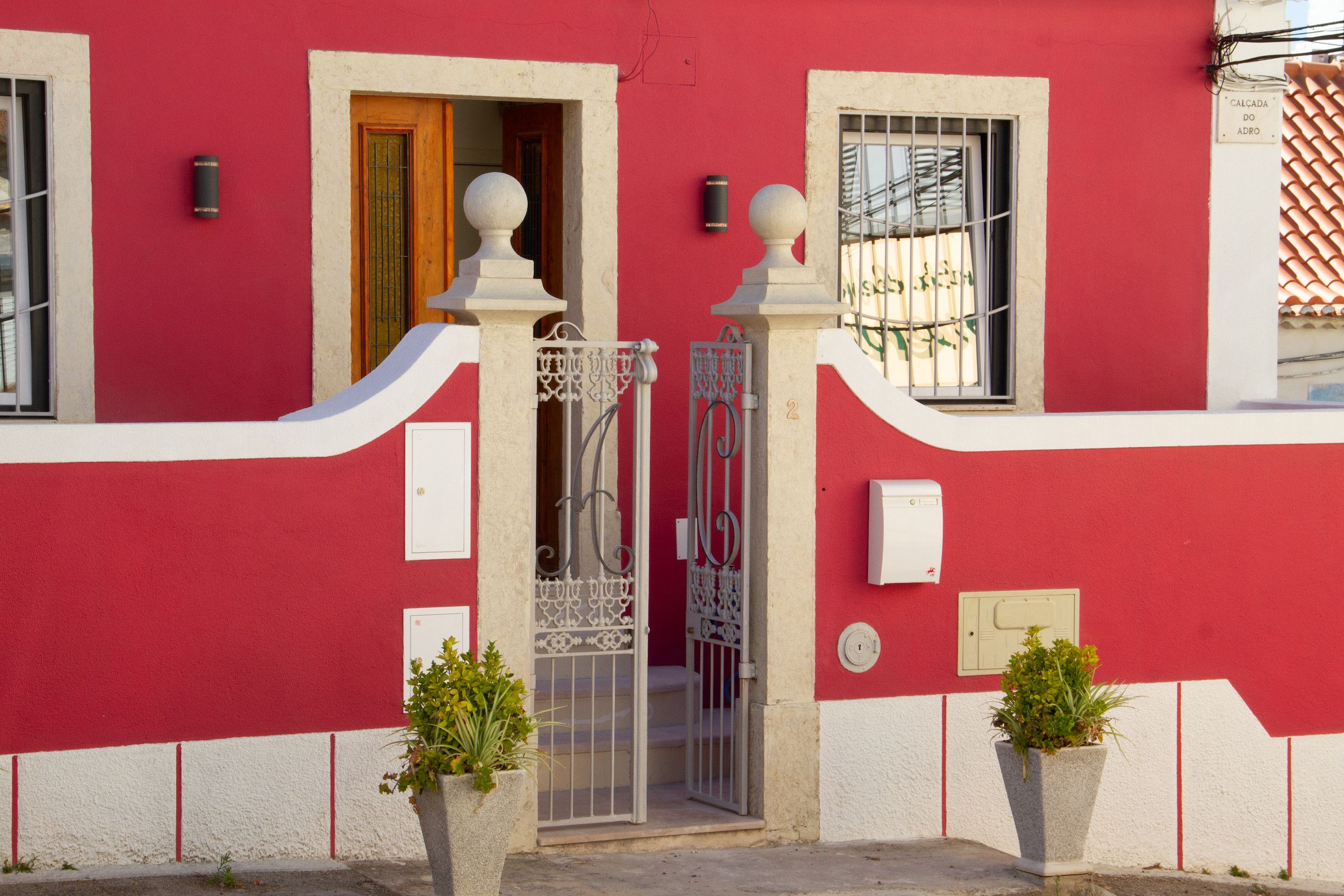 Um edifício vermelho com porta branca, um portão de metal e duas plantas em vasos.