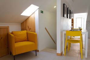 A room with a yellow chair, a white table, and a wooden door. - Loft with terrace and river view in Seixal. Air conditioning. Ideal for 2pax. (Seixal)
