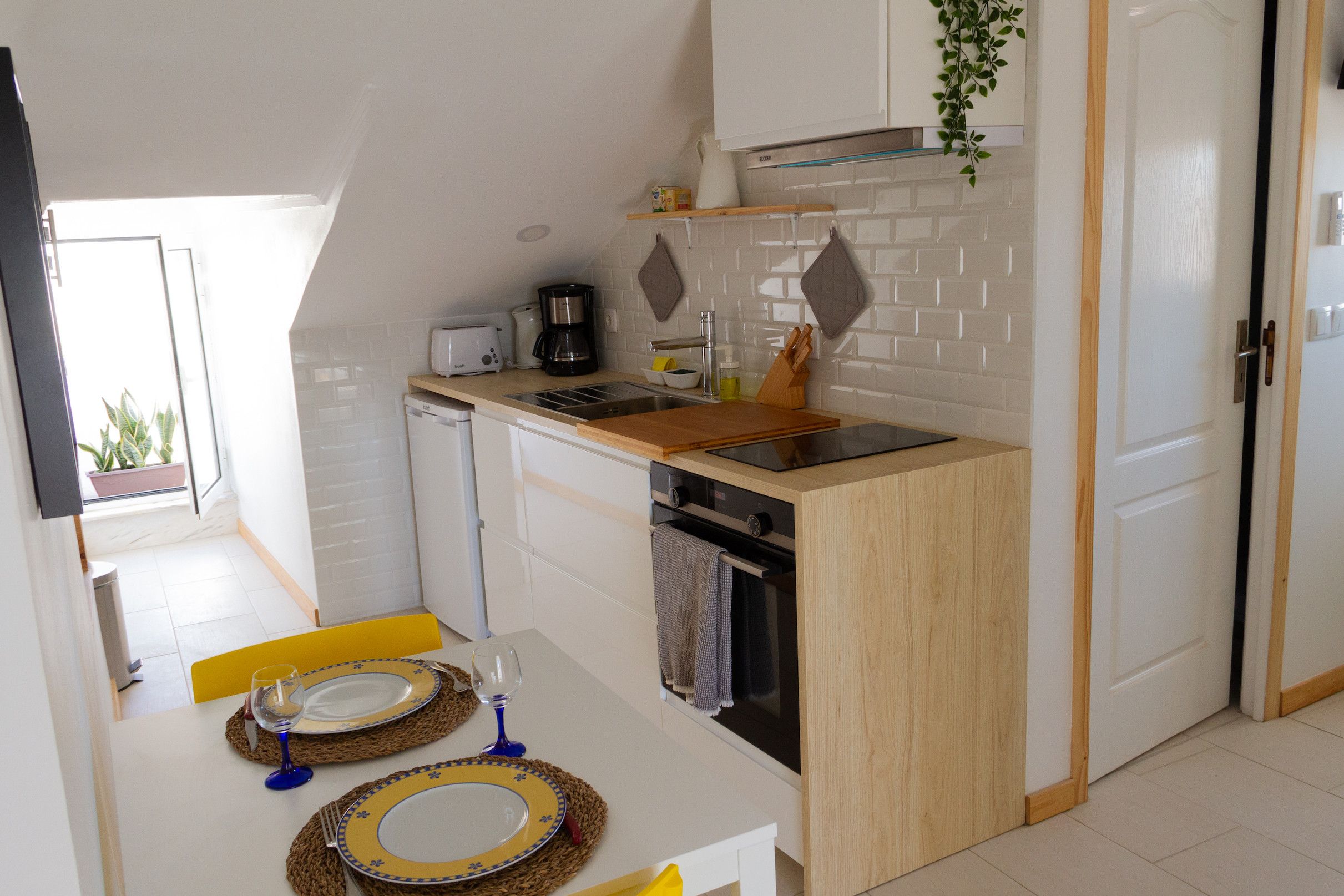 A compact kitchen with white cabinetry, a wooden countertop, and a dining area with a table set for two.