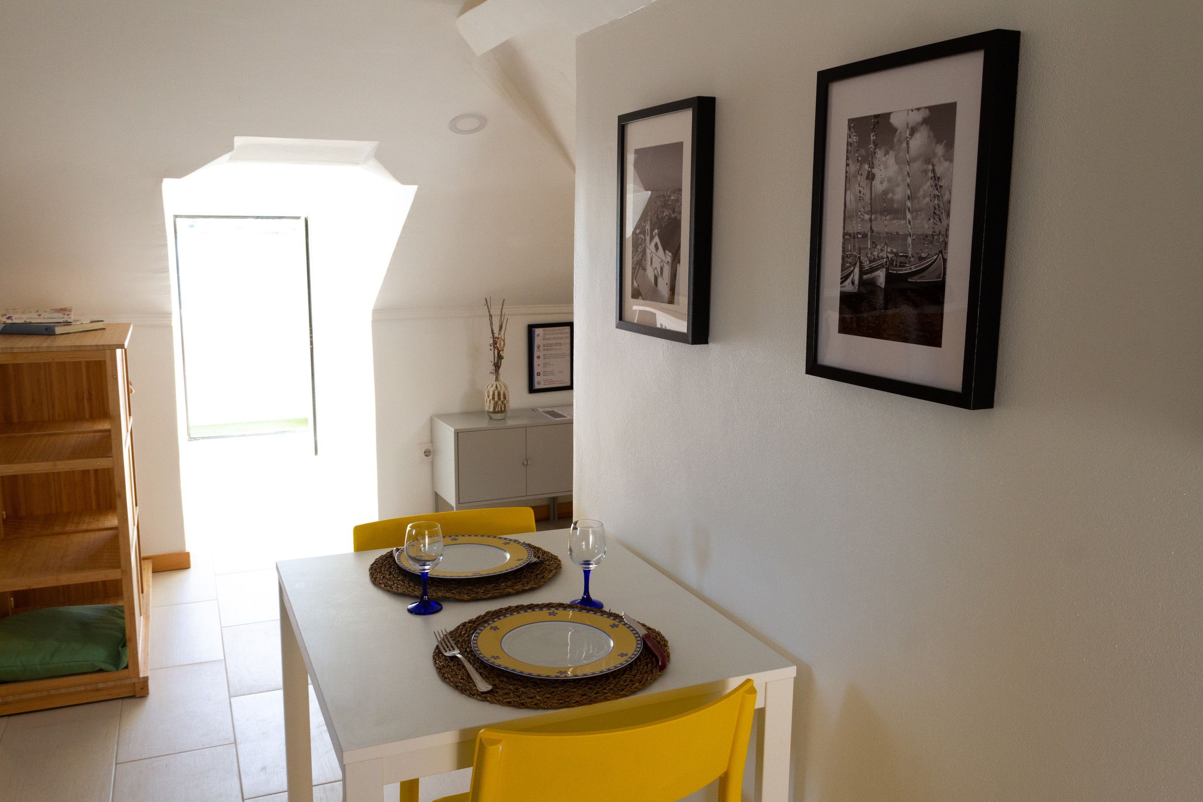 Un coin repas avec une table blanche dressée pour deux personnes, deux chaises et deux verres à vin.