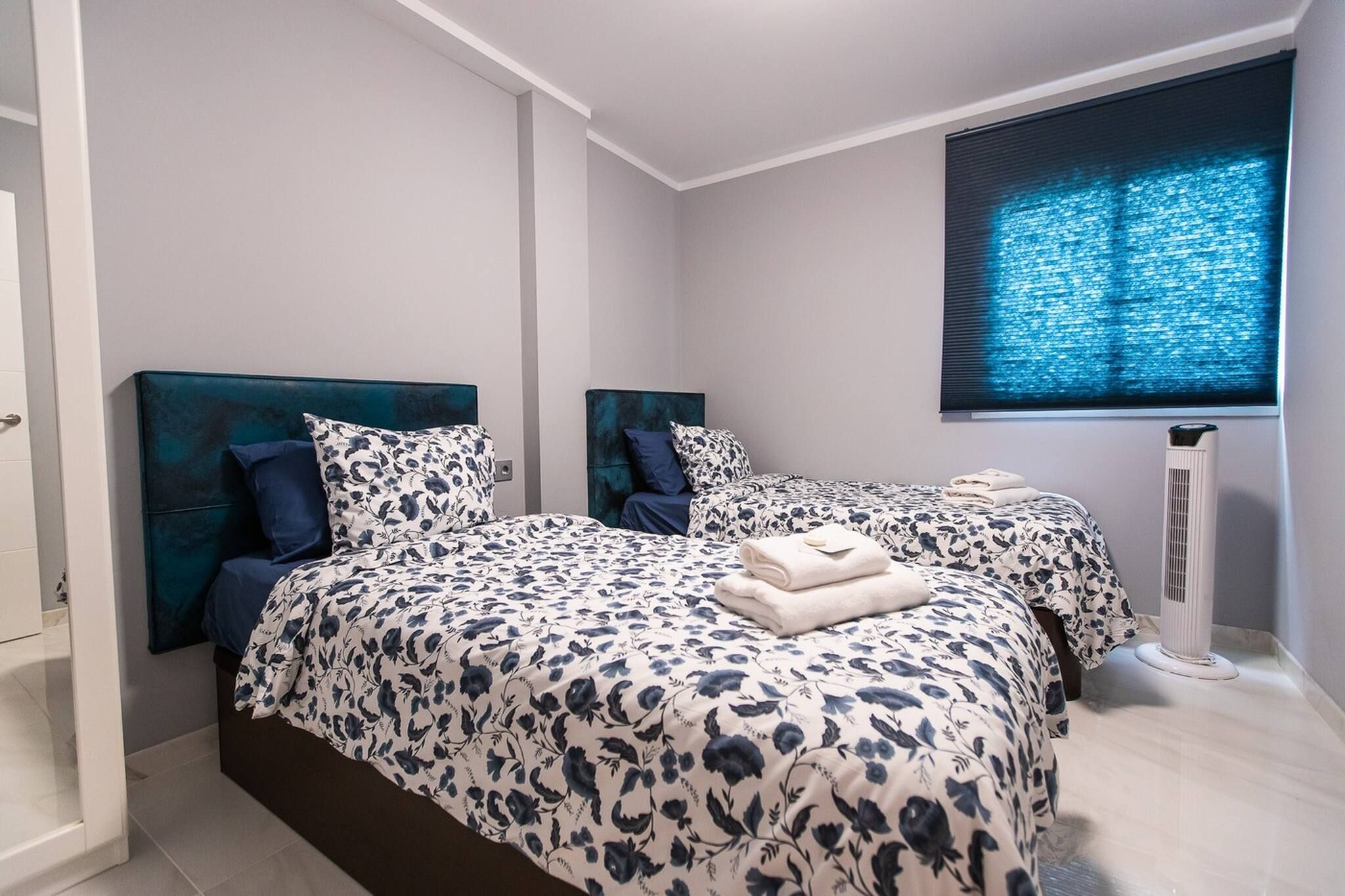 A bedroom with two beds, a window with blinds, and a standing heater.