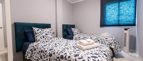 A bedroom with two beds, a window with blinds, and a standing heater.