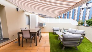 Une terrasse avec une table et des chaises, un ensemble de meubles de salon et un appareil de climatisation.