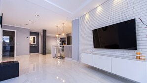 Un salon moderne doté d’un grand téléviseur à écran plat fixé sur un mur en briques blanches, d’un meuble de rangement élégant en dessous et d’un sol en marbre poli.