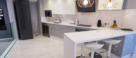 Una cocina moderna con encimera blanca, electrodomésticos de acero inoxidable e iluminación colgante.