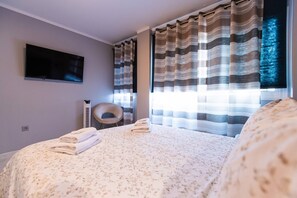 Une chambre à coucher avec un lit, une chaise, un téléviseur à écran plat et des rideaux.