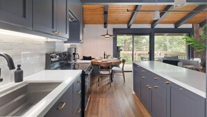 A modern kitchen with dark cabinets, a wooden ceiling, and a dining area with a table and chairs. - Condo with Parking and Smart TV! Steps to the Free Shuttle! (Mammoth Lakes)