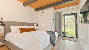 A bedroom with a large bed, wooden ceiling beams, a sliding glass door to a balcony, and a TV mounted on the wall. - Condo with Parking and Smart TV! Steps to the Free Shuttle! (Mammoth Lakes)