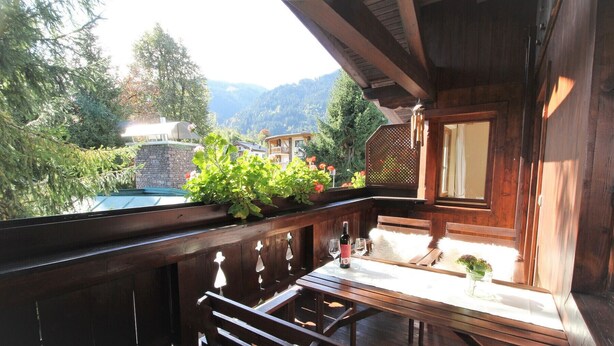 Ein Holzbalkon mit Tisch, zwei Stühlen und einer Weinflasche.