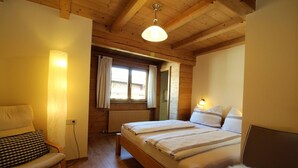 Ein gemütliches Schlafzimmer mit einem hölzernen Bett, einem Sessel, einem Fenster mit Vorhängen und einer Deckenleuchte.