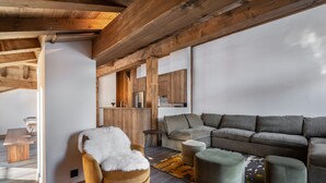 Un salon moderne avec un plafond en bois, un canapé, des poufs et un fauteuil recouvert d'un plaid en fourrure.