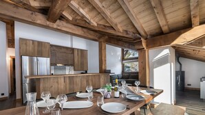 Une cuisine moderne avec des poutres en bois, des appareils en acier inoxydable et un coin repas aménagé pour six personnes, avec des verres à vin et des assiettes.