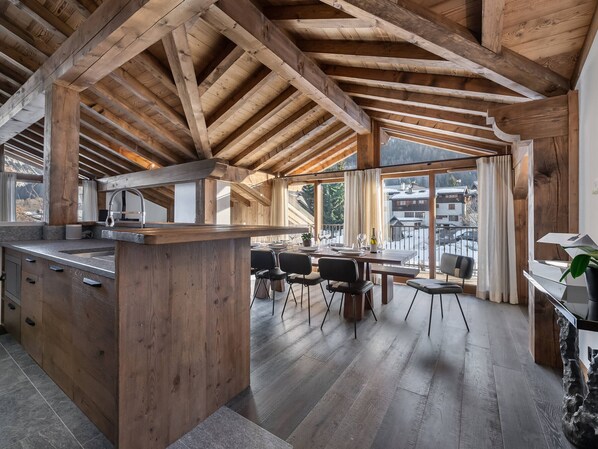 Une cuisine spacieuse avec des poutres en bois, un grand îlot central et un coin repas offrant une vue sur les montagnes.