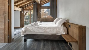 Une chambre avec un plafond en bois, un lit recouvert de draps blancs, une fenêtre avec des rideaux et une vue sur l’extérieur.