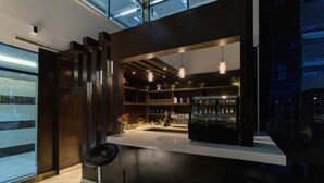 Un espace bar moderne avec un comptoir blanc, des luminaires suspendus et un réfrigérateur noir.