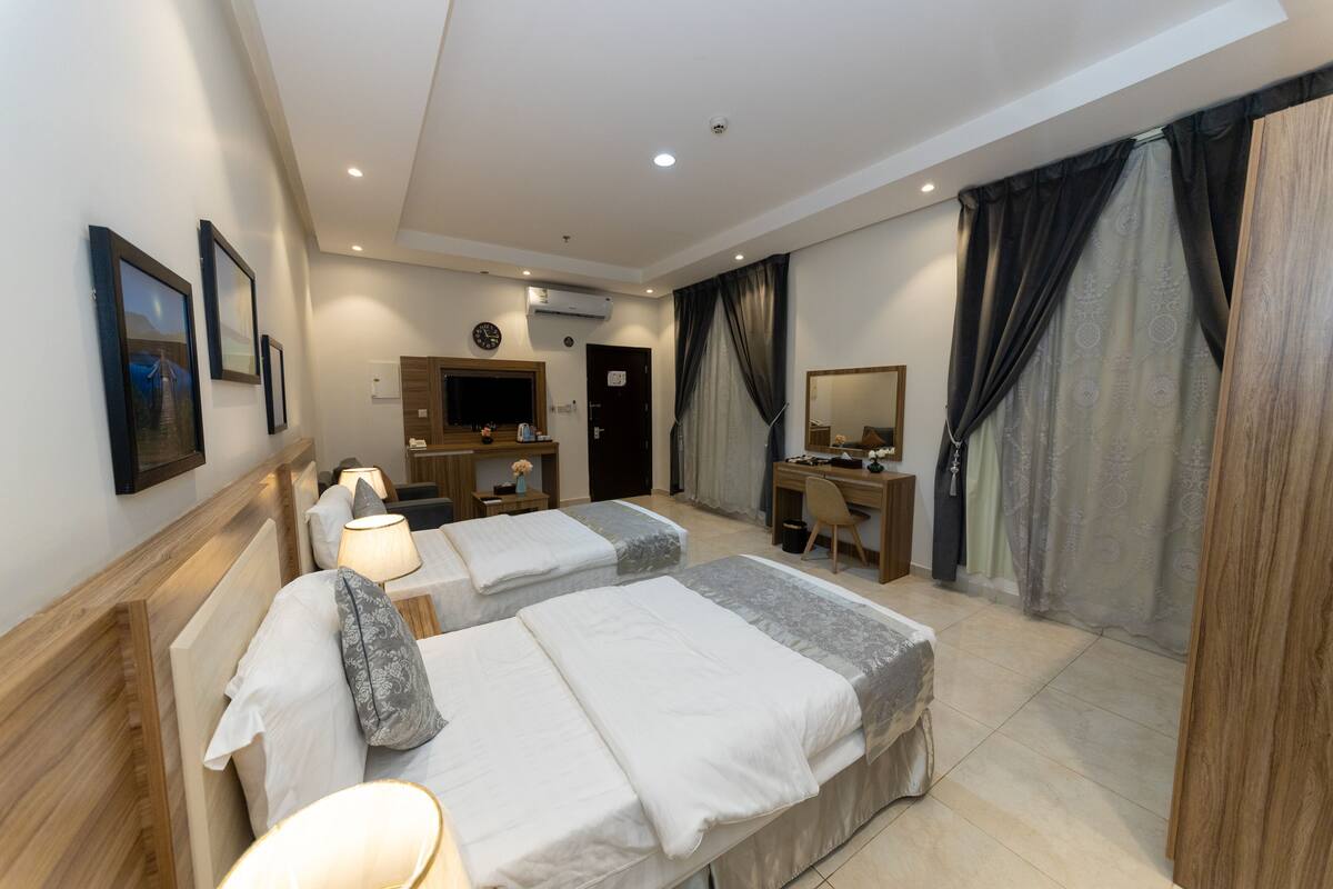 A hotel room with two beds, a desk, a chair, a mirror, and a wardrobe.