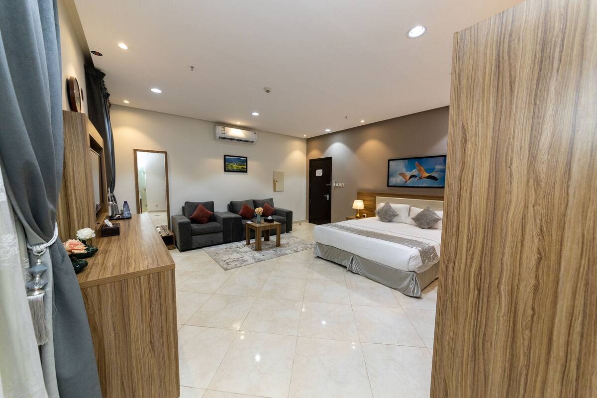 A hotel room with a bed, two sofas, a small table, and a mirror.