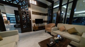 Un hall d’entrée moderne avec un canapé, un fauteuil et une table basse, un téléviseur posé sur un meuble et un mur orné d’un motif.