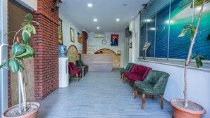 Zona de recepción con pared de ladrillo, dispensador de agua y mostrador de recepción. Hay dos sillones verdes y una silla roja.
