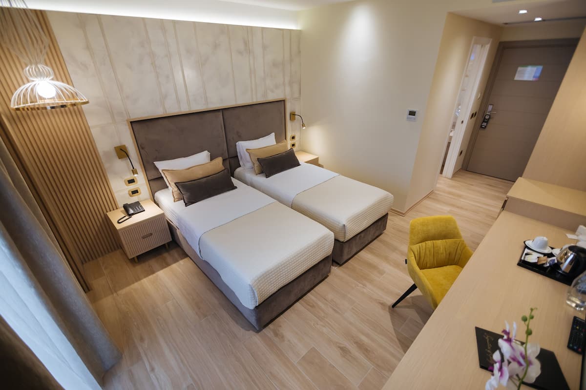 Una habitación de hotel moderna con dos camas, un escritorio, una silla amarilla y suelo de madera.