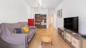 Een moderne woonkamer met een bank, televisie, boekenkast en een rieten fauteuil.
