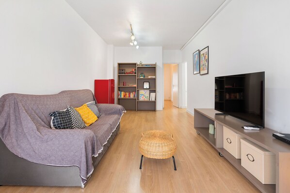 A modern living room with a sofa, television, bookshelf, and a wicker chair.