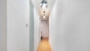 Een smalle gang met witte wanden en houten vloer, die leidt naar een kamer met een bed en een raam.