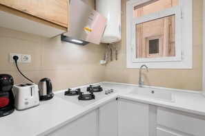 A kitchen with a gas stove, a toaster, a kettle, a water heater, and a window with a view of the outside.