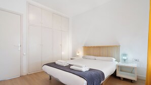 Een hotelkamer met een bed, nachtkastje, kledingkast en een nachttafeltje met een lamp.