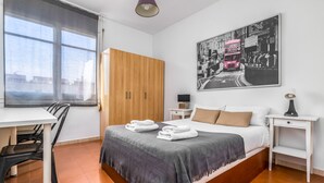 Quarto moderno com cama, escrivaninha, guarda-roupa e uma janela grande.