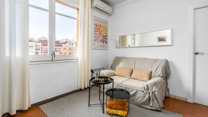 Uma sala de estar moderna com um sofá bege, uma mesa redonda pequena com uma chaleira, um tapete e um cartaz de Henri Matisse.