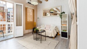 A cozy living room with a sofa, a small table, a bookshelf, and a window with blinds. - Wake in a luminous, chic and ideally located flat, surrounded by the magic of Barcelona (Barcelona)