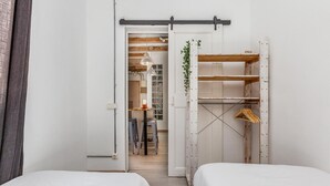 A bedroom with two beds, a wooden wardrobe, and a hallway leading to a bathroom. - Wake in a luminous, chic and ideally located flat, surrounded by the magic of Barcelona (Barcelona)
