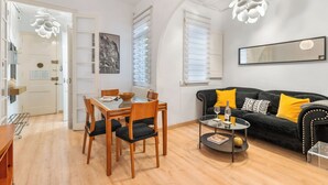 Ein modernes Wohnzimmer mit Essbereich, einem schwarzen Sofa mit gelben Kissen, einem Glastisch und einem großen Spiegel an der Wand.