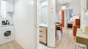 Eine moderne Küche mit Waschmaschine, ein Essbereich mit Tisch und Stühlen sowie ein sichtbares Badezimmer mit Waschbecken und Spiegel.